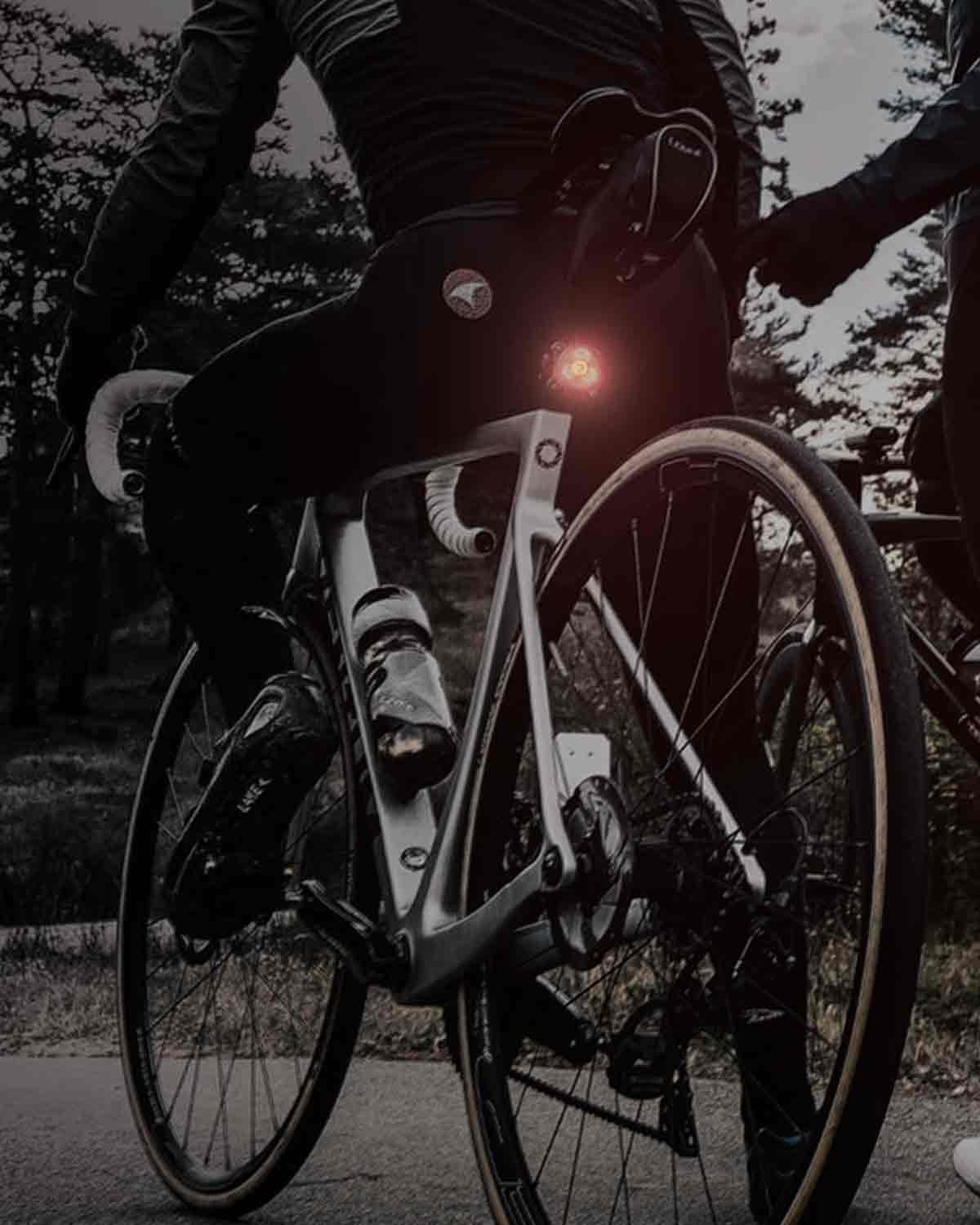 The bottom half of 2 bicycle riders stopped on the side of the road with bright rear lights mounted on their seat posts.