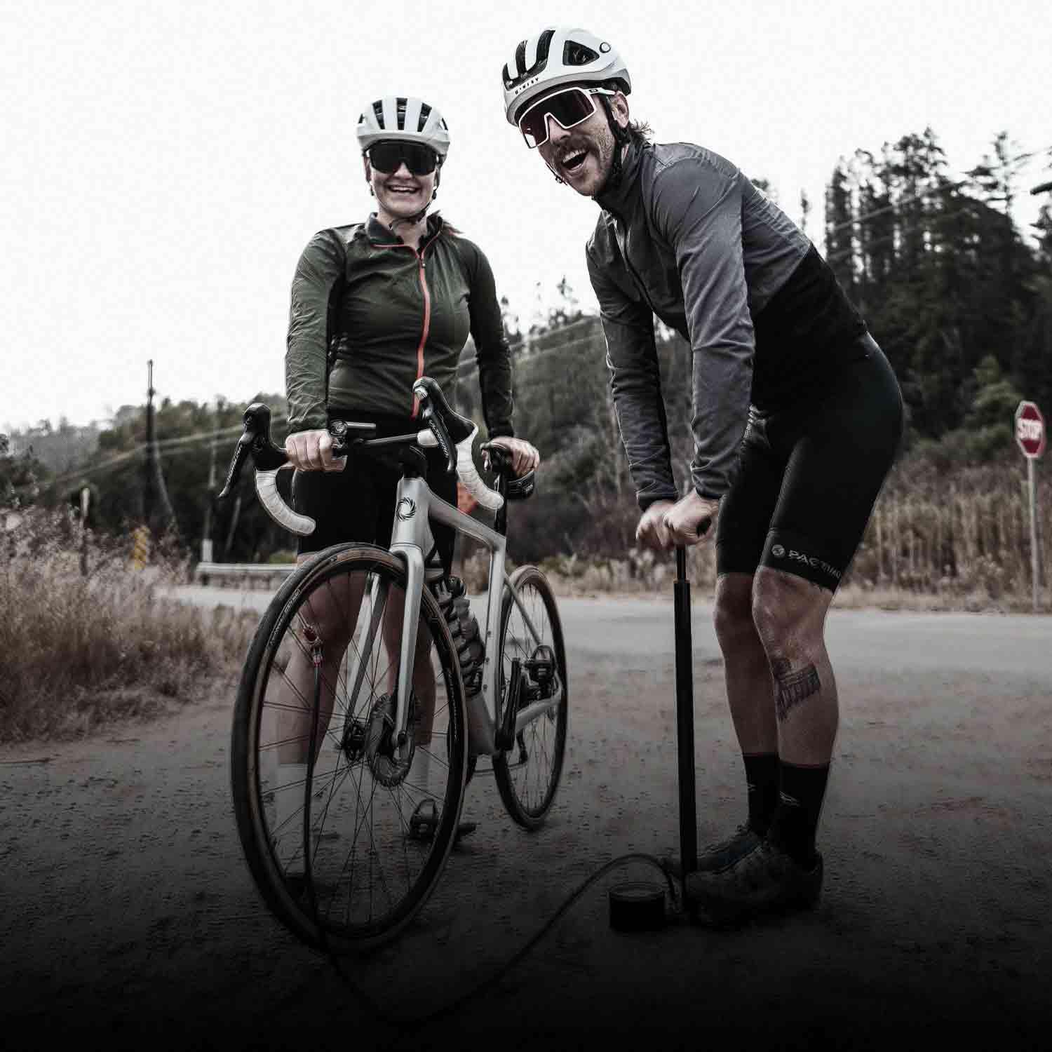 2 people standing next to a bicycle using a floor pump to inflate the tire.