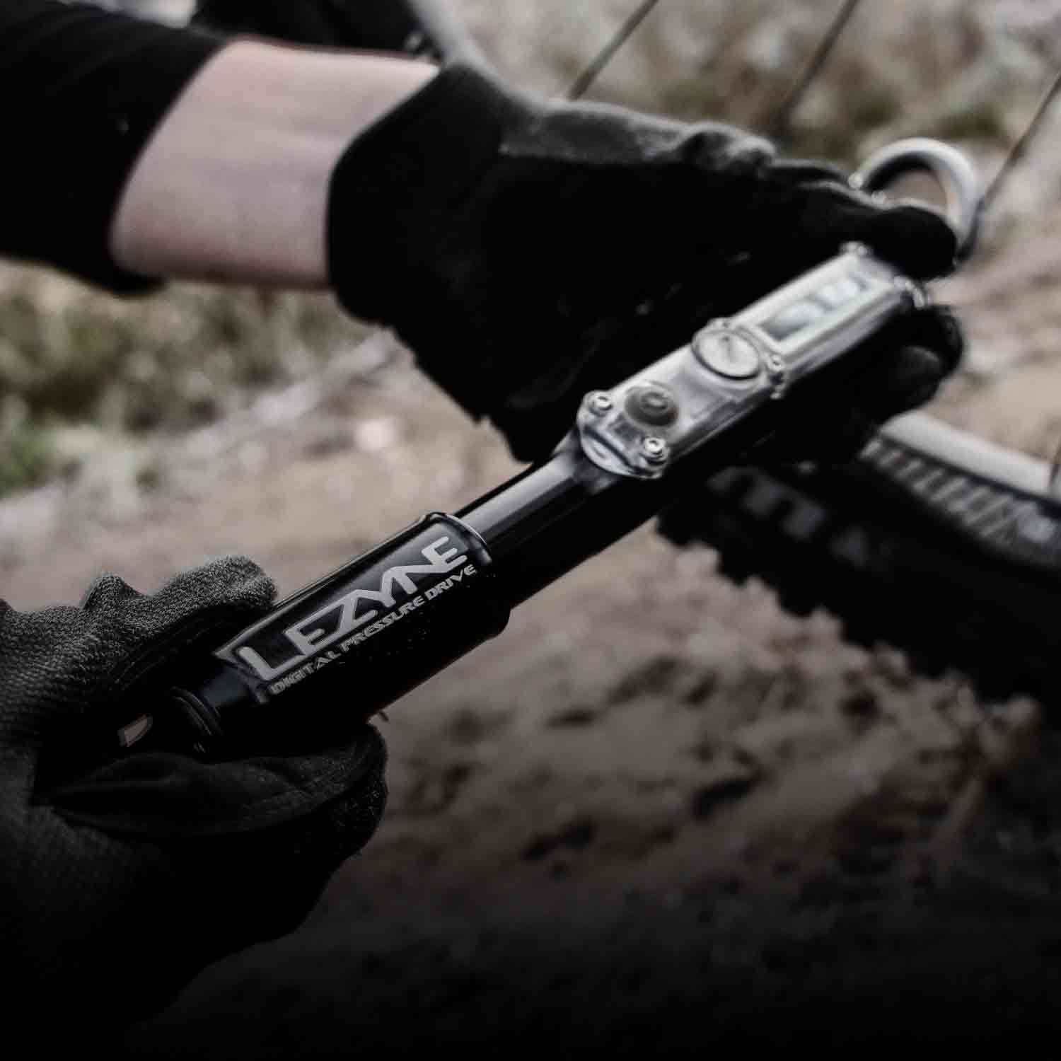 Gloved hands holding a hand pump while inflating a mountain bike tire.