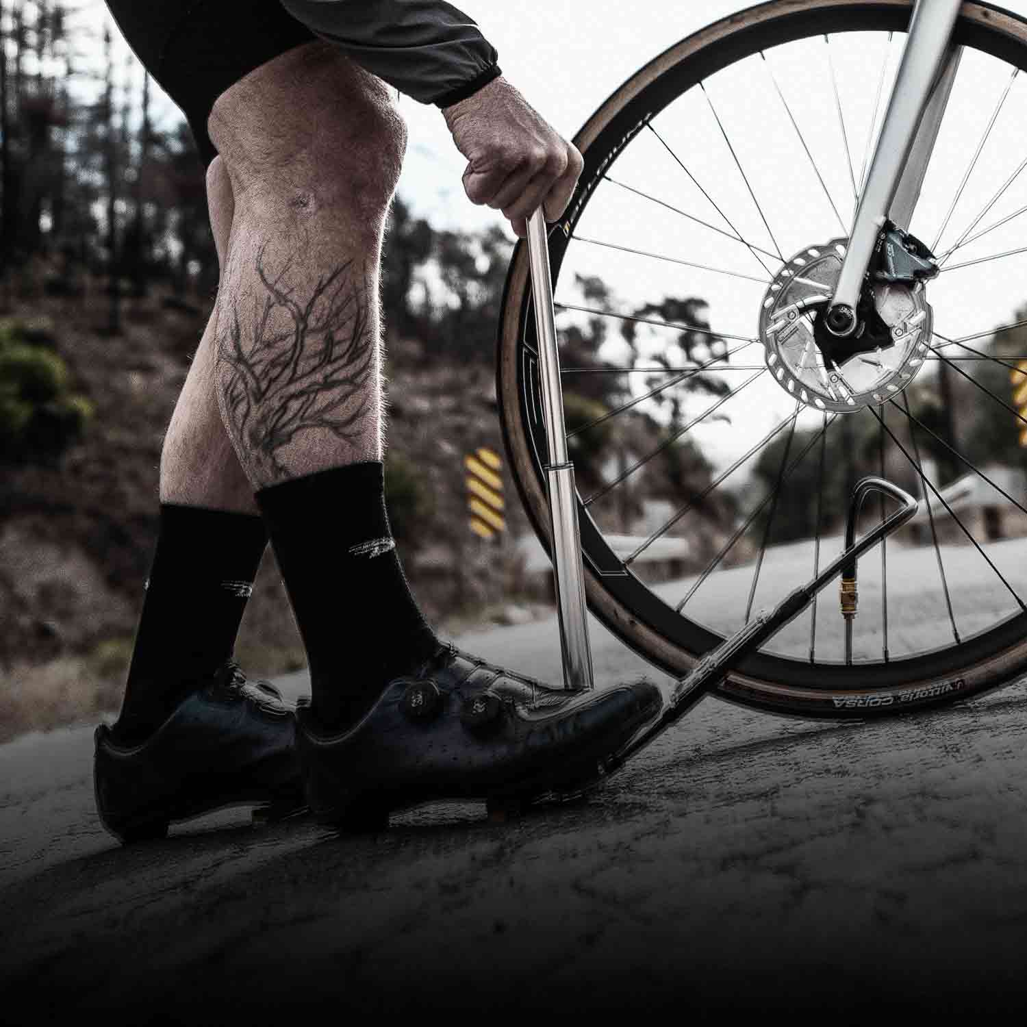 Someone using a small pump to inflate a road bike tire while holding the pump to the ground with their foot.