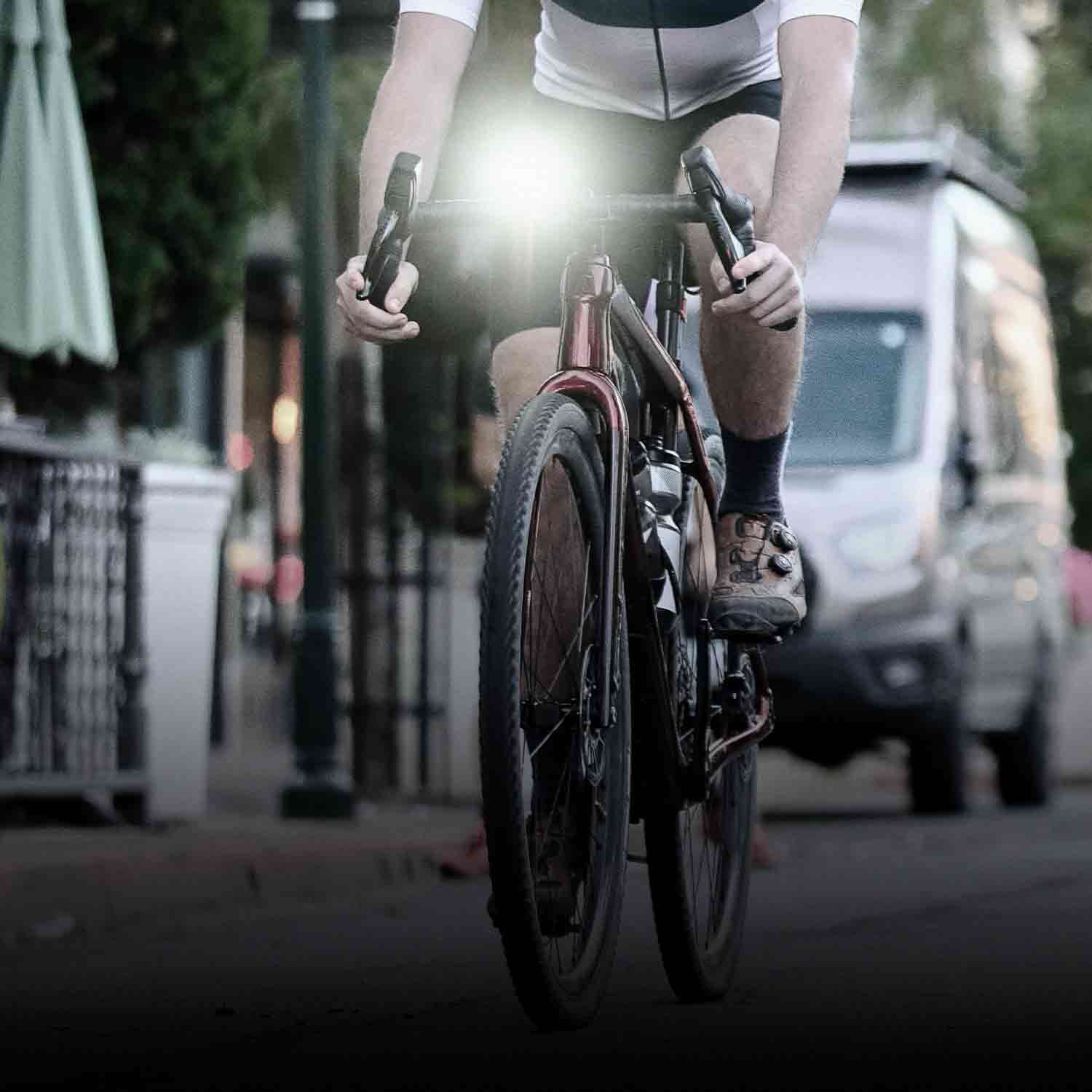 A bright front lite mounted on a bicycle being ridden in light traffic on a road.