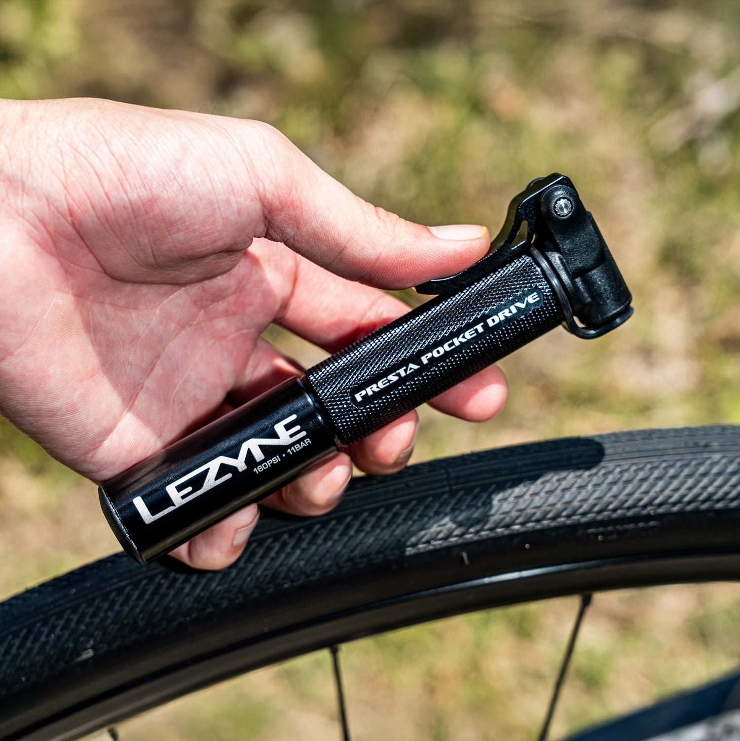 Cyclist using the Presta Pocket Drive bike hand pump on a gravel bike tire, highlighting on-the-go inflation ease.