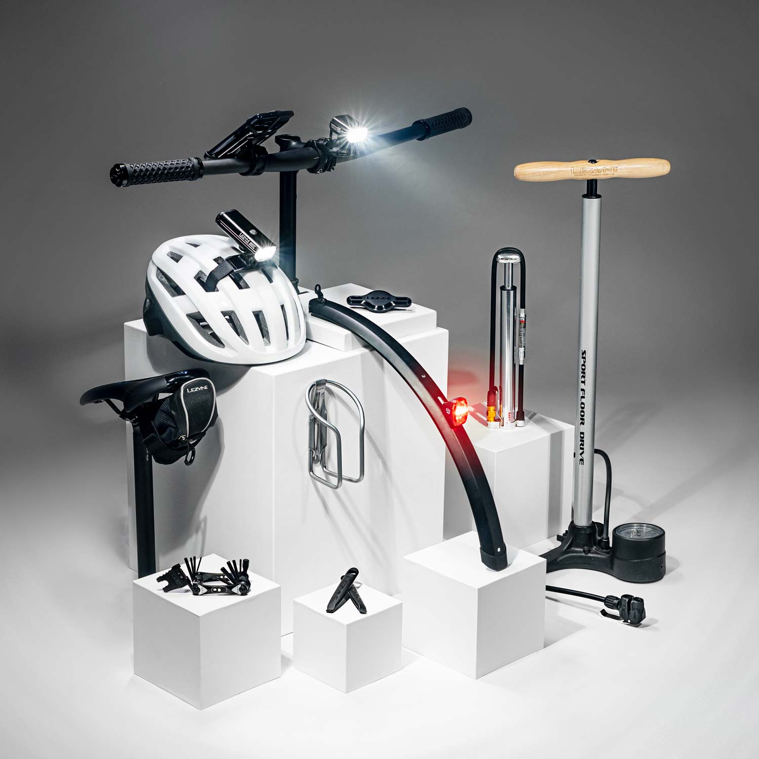 Bicycle tools, bags, lights pumps, and mounts on display podiums with the parts of a bicycle that they attach to. 