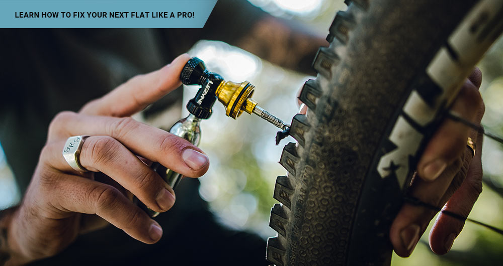 A cyclist holding a Lezyne Tubeless CO2 Blaster in the midst of a trail, ready to repair a flat tire with the compact, lightweight, and efficient tool designed for quick tire inflation and puncture sealing.