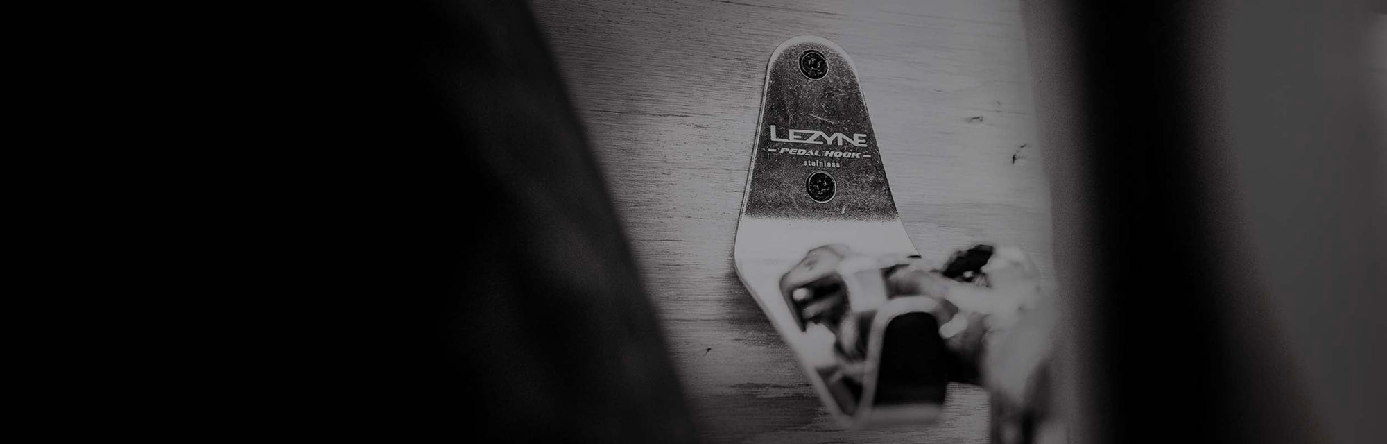 A close up of a metal bracket mounted to a wall with the words Lezyne Pedal Hook Stainless printed on it.