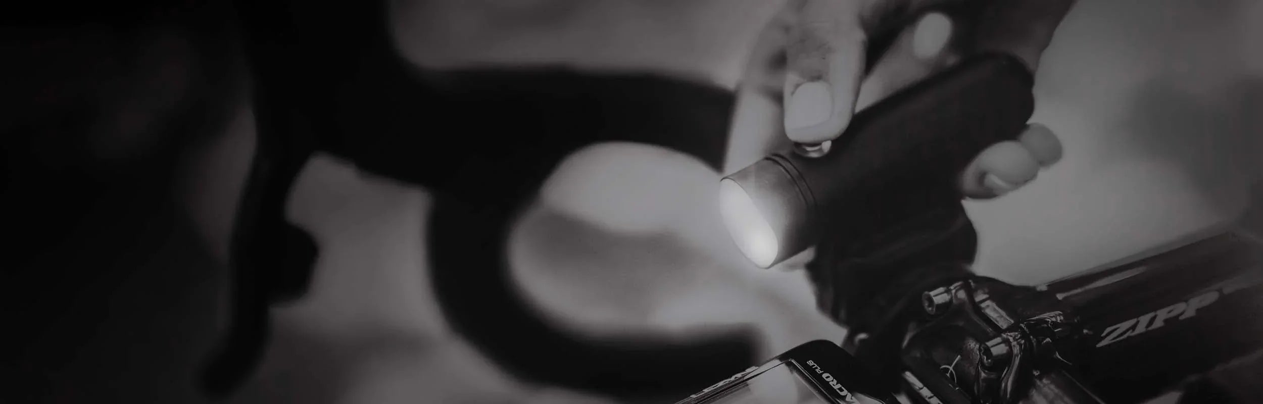 Person pressing the power button on a front bike light mounted on bicycle handlebars.