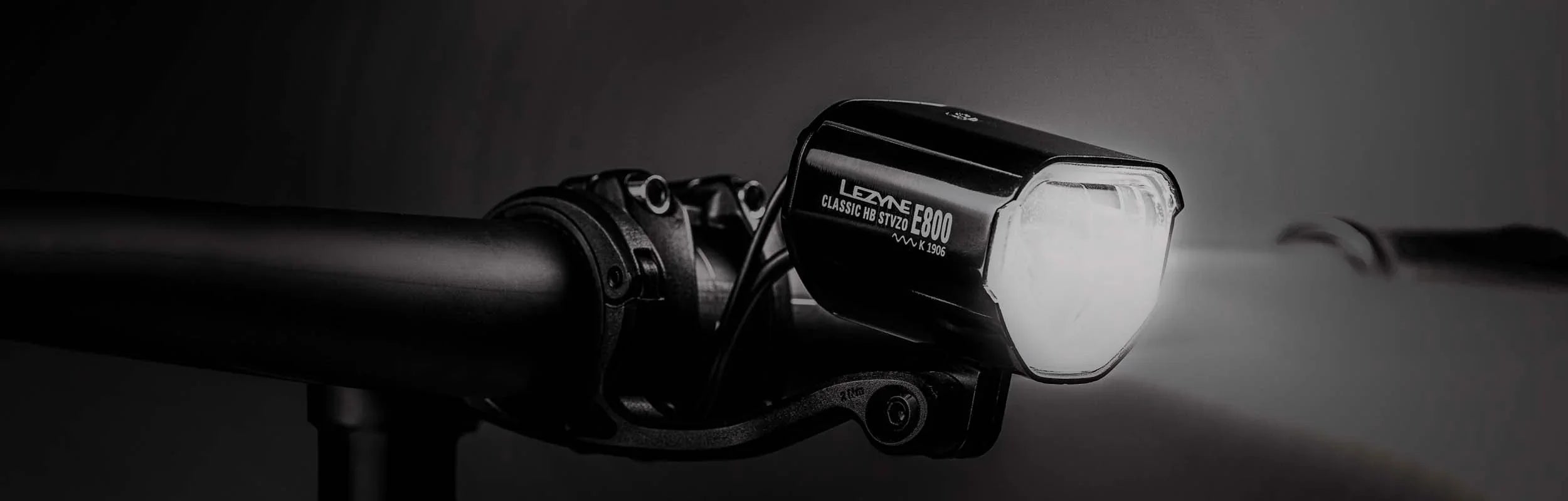 Handlebar-mounted Lezyne Classic HB STVZO E800 K 1906 bike light, highlighting the model name printed on its side.