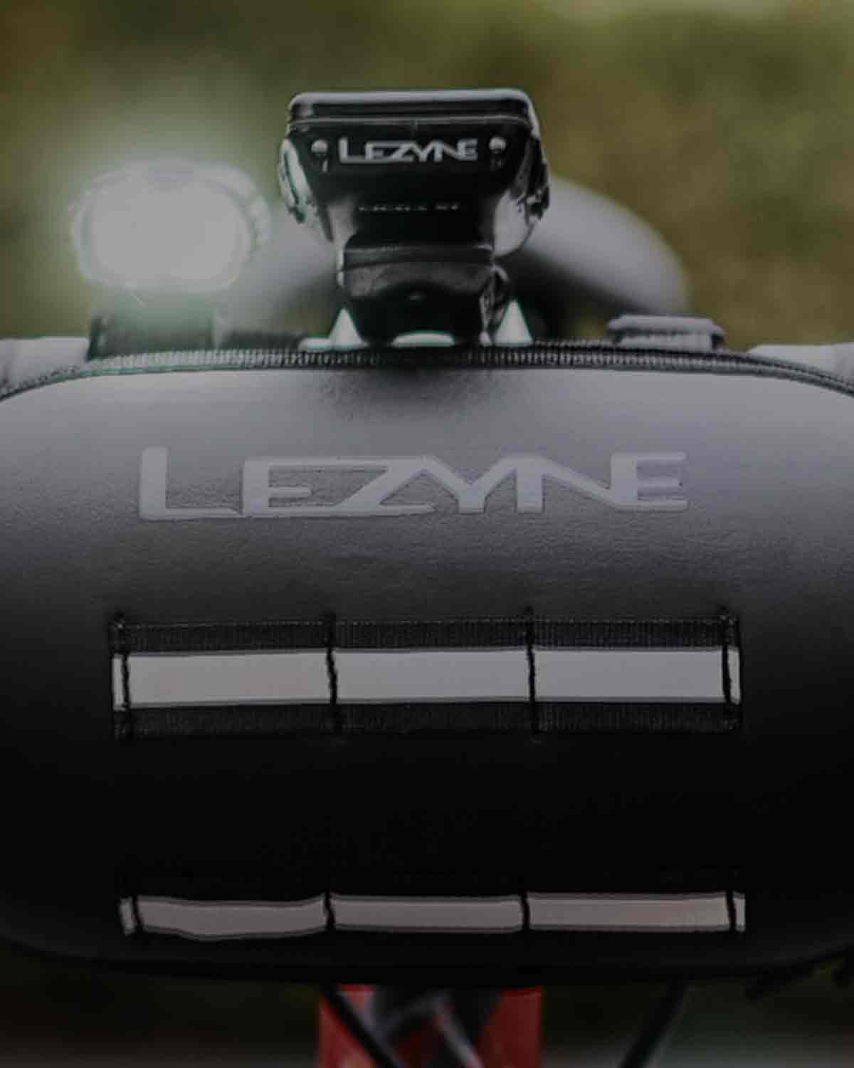 A bag mounted to bicycle handlebars with the word Lezyne printed on it.
