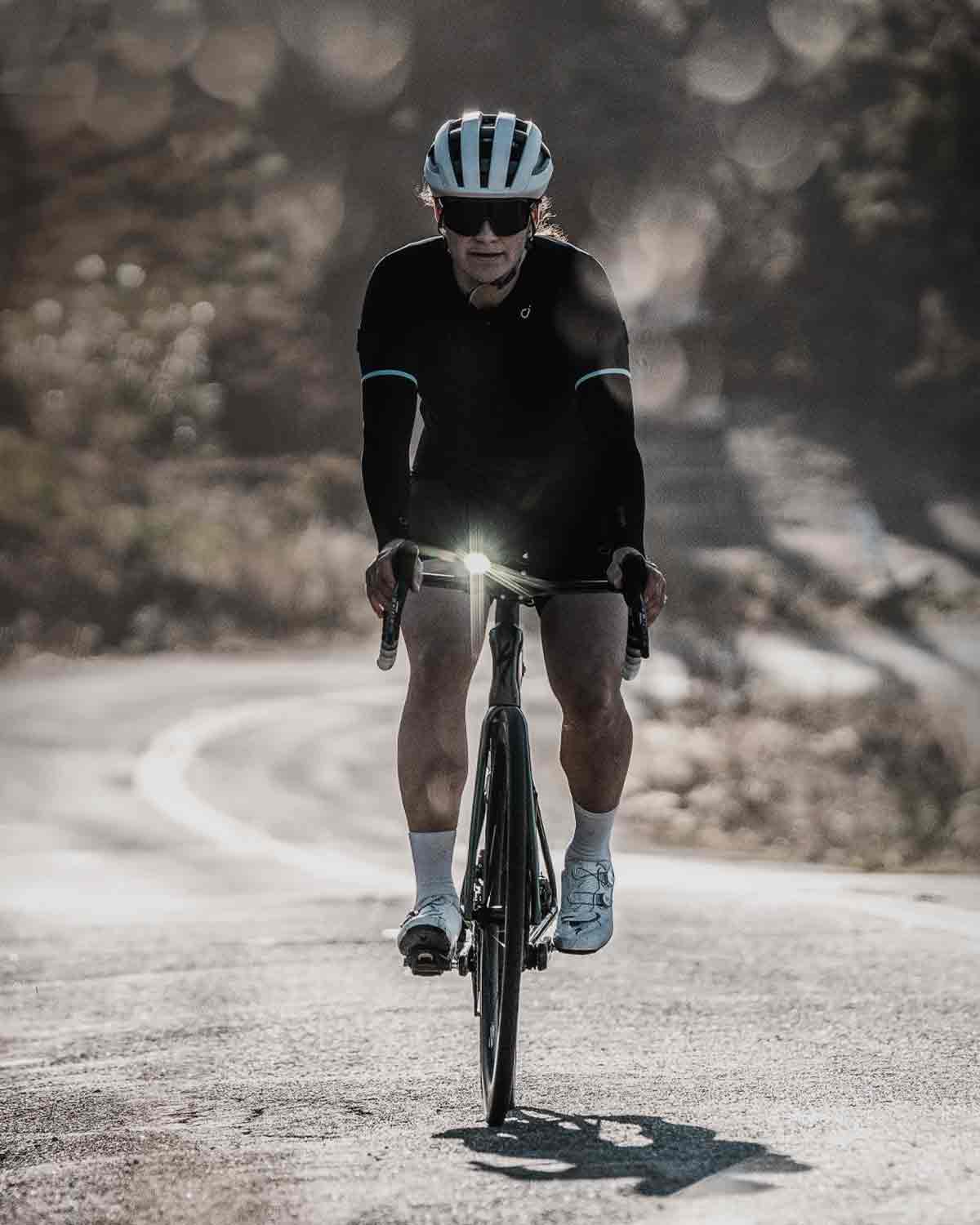 A person riding a bicycle on a road with a bright front light mounted on the handlebars. 