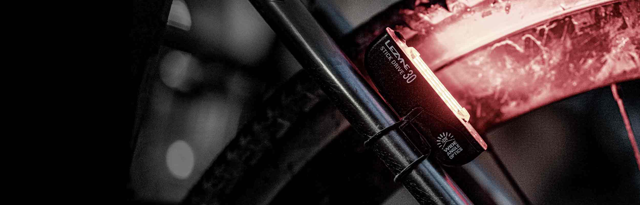 A close up of a light mounted on the rear of a bicycle that is illuminating the bicycle tire. The words Lezyne Stick Drive 30 are printed on the side of the light.
