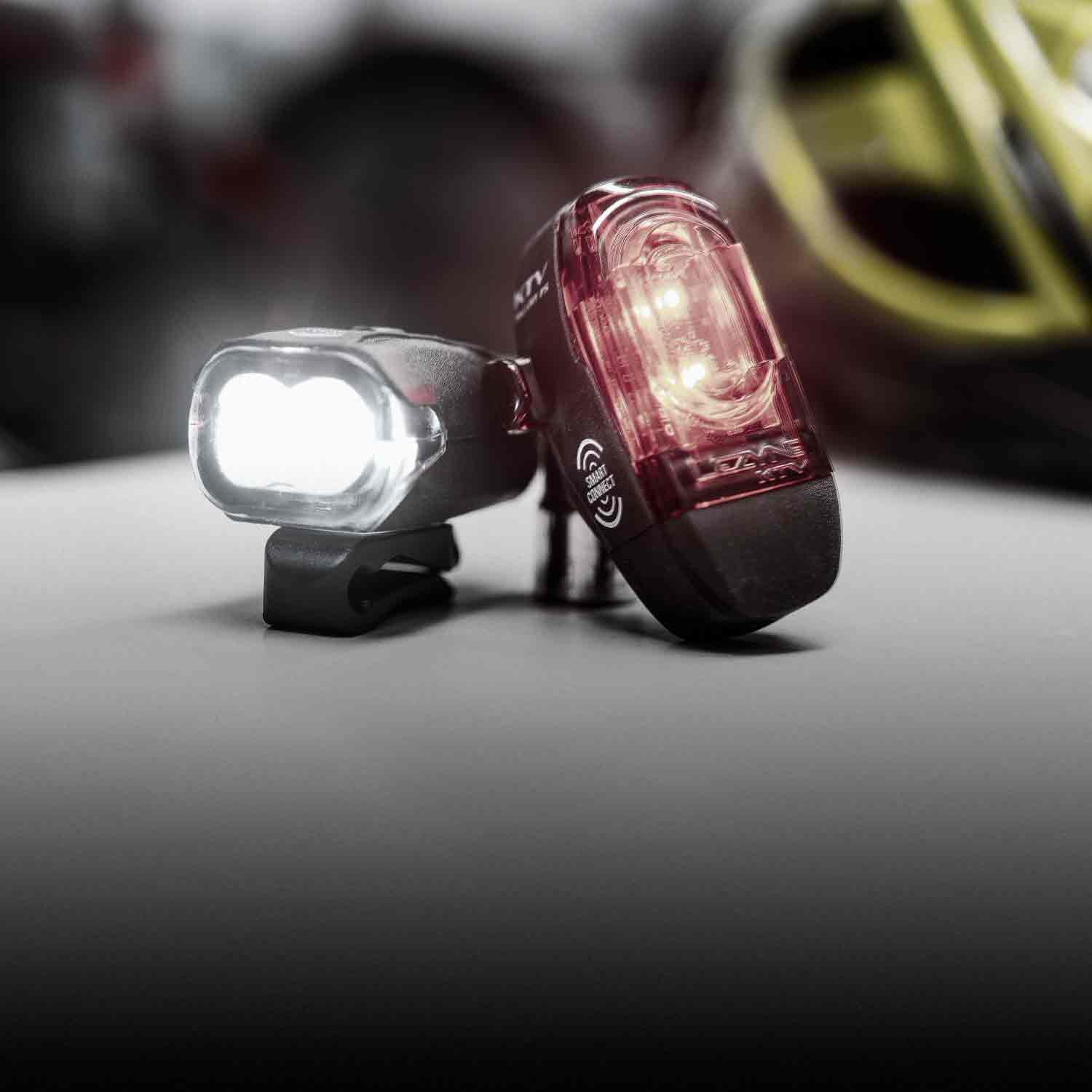 A front and a rear bicycle light on a surface. One of the lights has KTV Smart Connect printed on the side.