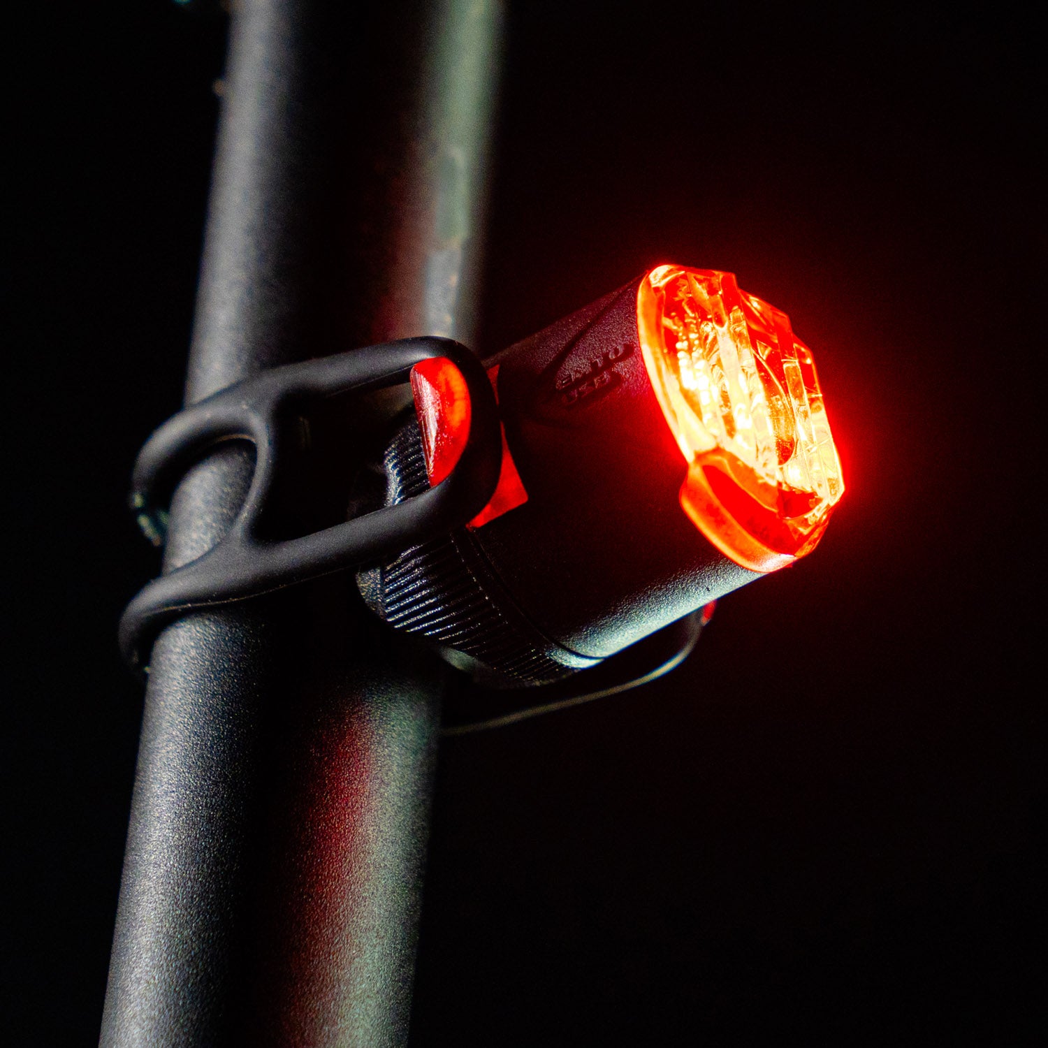 Close-up side view of the circular Lezyne Femto USB Rear StVZO LED taillight, emitting a strong red light, mounted on the seat post.