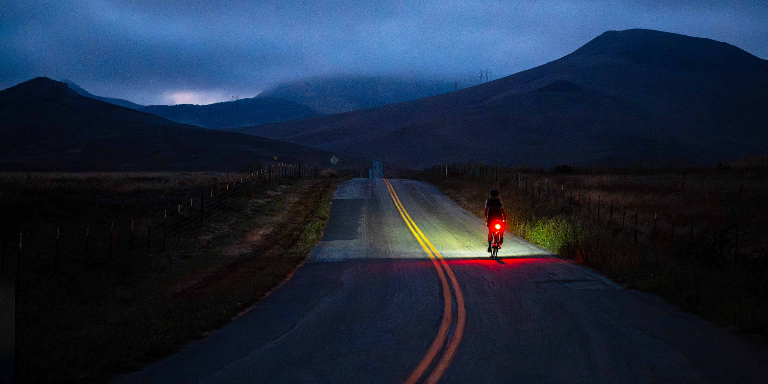 Cyclist on the road in the dark with front leading the way and bright taillight 