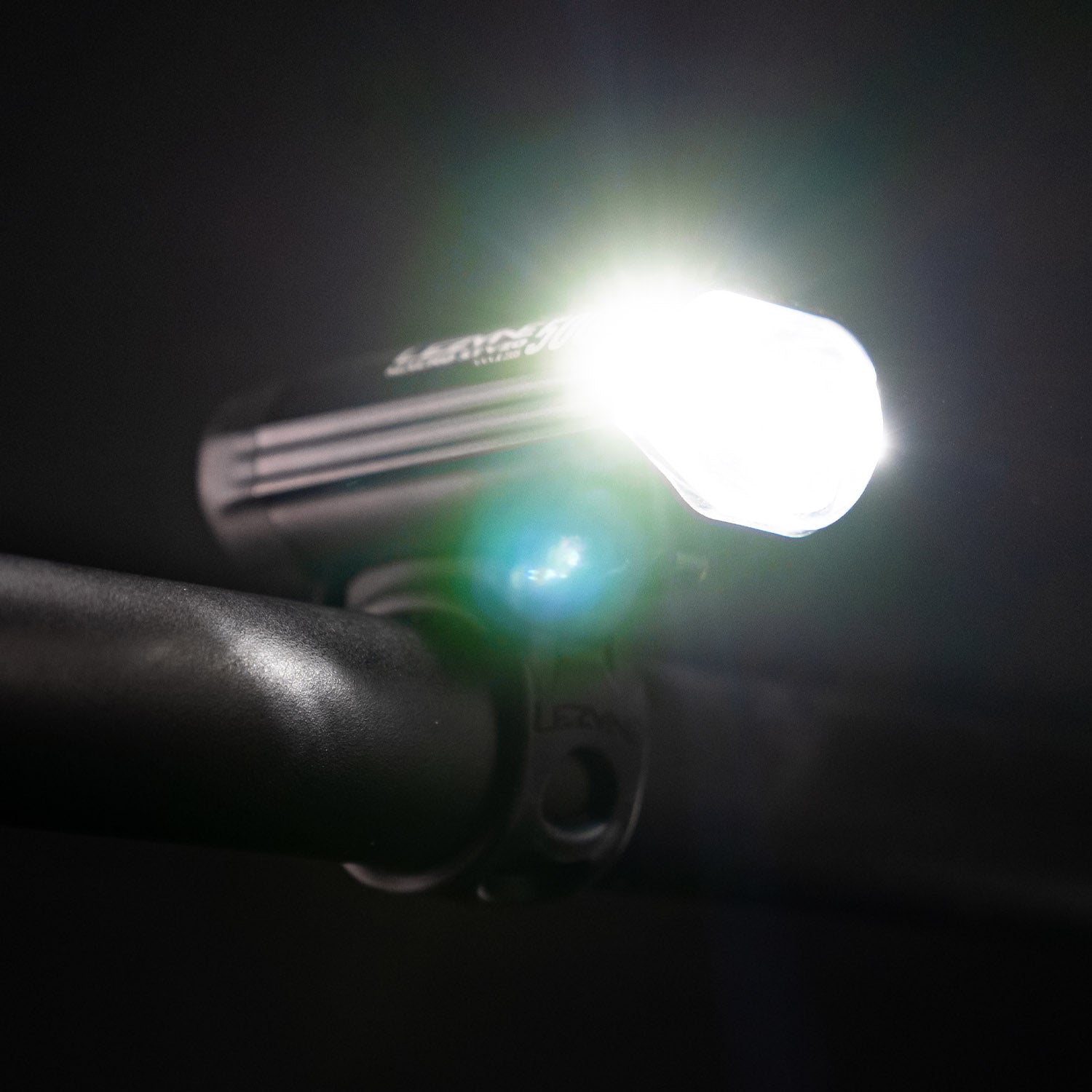Upward view of the Lezyne Macro StVZO 500+ headlight, angled to the right and emitting a bright white beam, mounted on the handlebars.