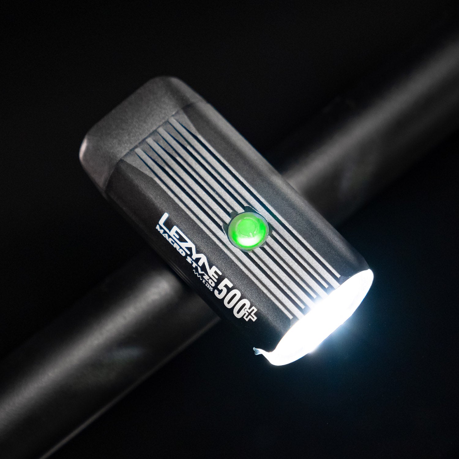 Bird's-eye view of the Lezyne Macro StVZO 500+ LED light, angled downwards to the right, with a green circular power light on top, mounted on the handlebars.