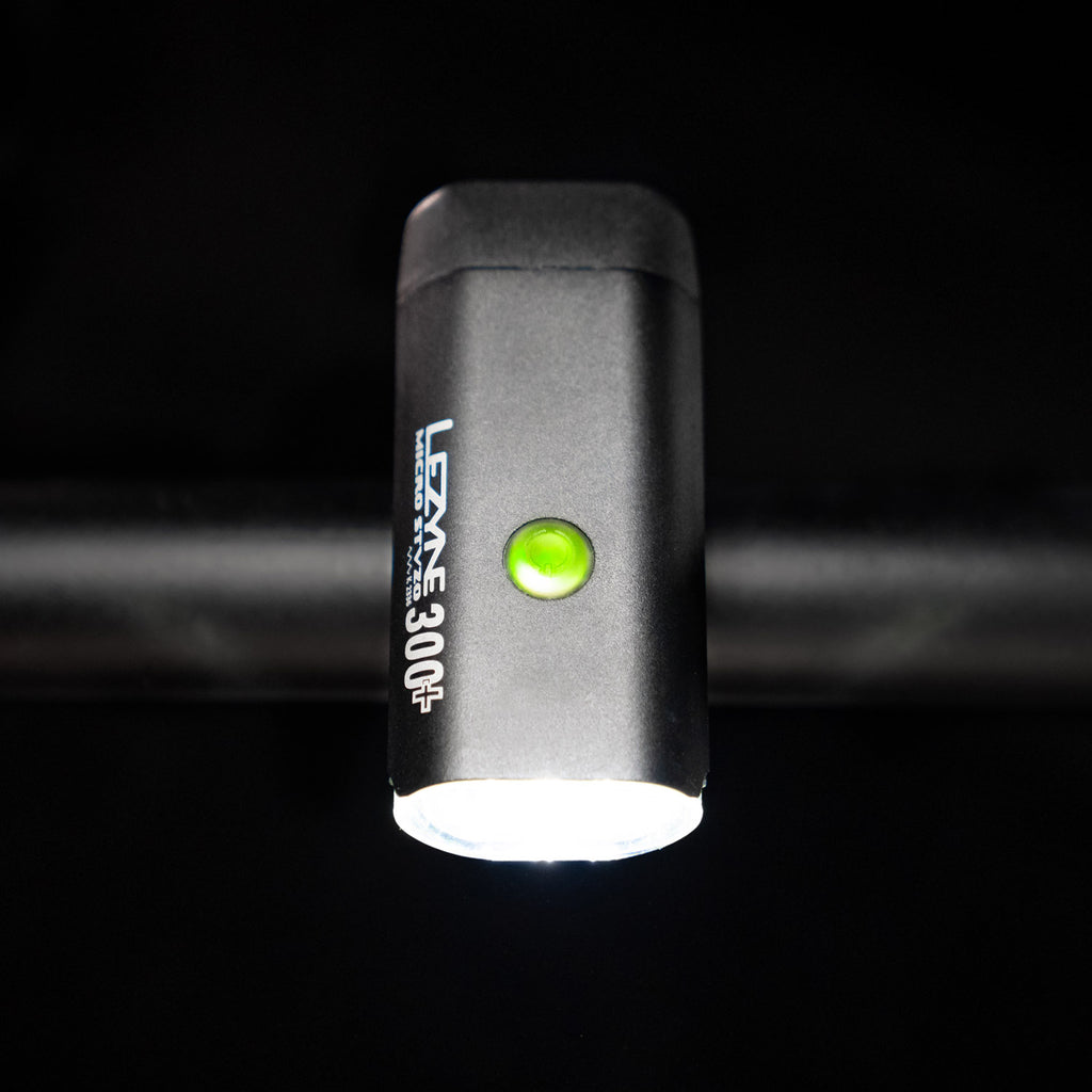 Top-down view of the Lezyne Micro StVZO 300+ headlight with a green lit power button on top of the housing, mounted on the bike handlebars.