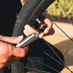 Cyclist inflating tire of his gravel bike using the CO2 chuck of the Pocket Drive CO2 bike hand pump, demonstrating fast inflation on the go. Schrader valve and Presta valve compatible.